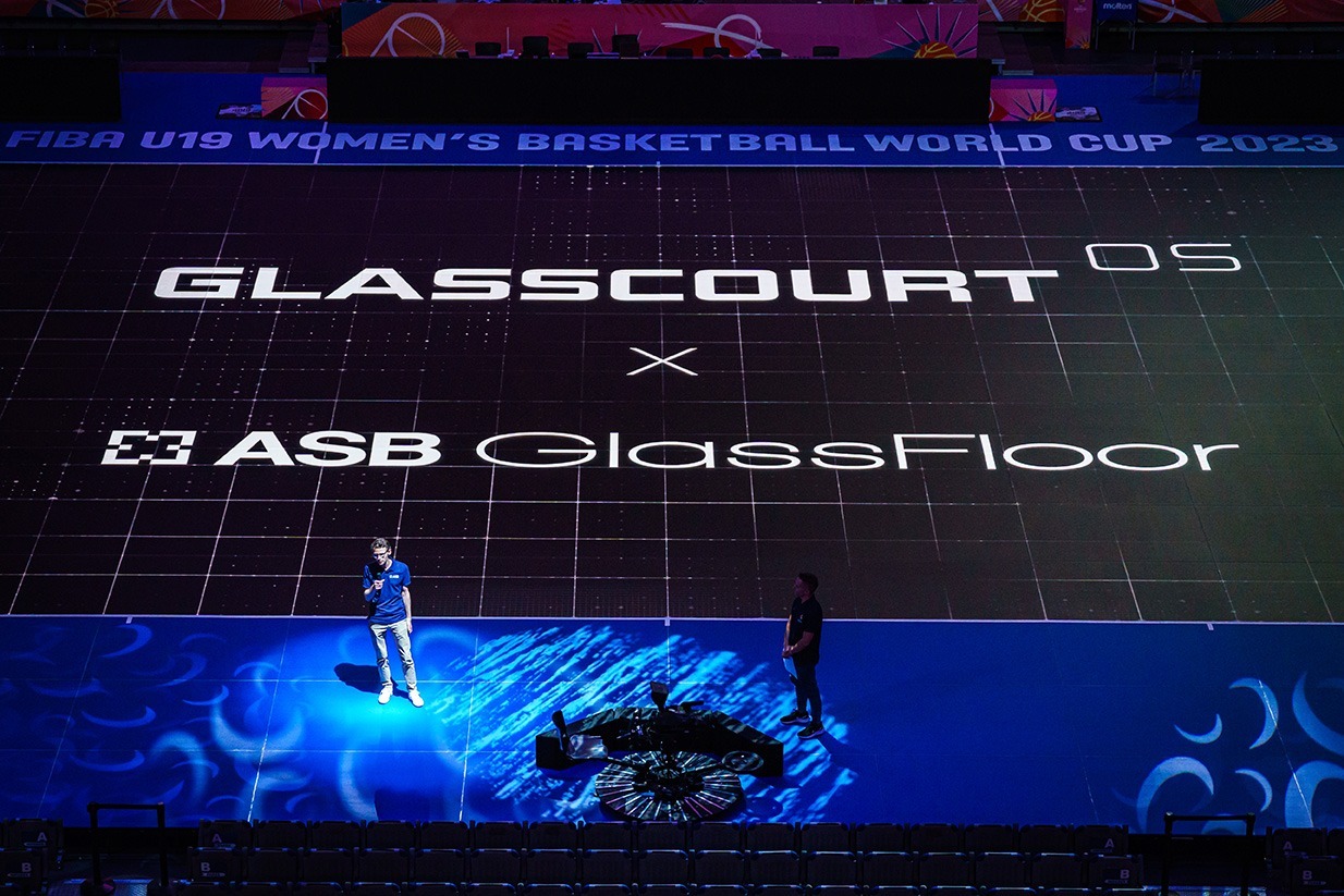 Zwei Personen stehen auf beleuchtetem LED-Glasboden mit großem „GlassCourt OS x ASB GlassFloor“-Logo.
