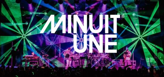 Das Bild zeigt eine beeindruckende Live-Bühnenszene mit einer dynamischen Lichtshow. Der Hintergrund ist von intensiven grünen und violetten Lichteffekten geprägt, die strahlenförmig von verschiedenen Punkten ausgehen und den gesamten Raum einhüllen.

In der Mitte des Bildes befindet sich das große, weiße Logo von Minuit Une, das prominent über die Szene gelegt wurde. Auf der Bühne stehen mehrere Musiker, die von einer aufwendigen Lichtinstallation umgeben sind.

Die Beleuchtung erzeugt eine immersive Atmosphäre, die typisch für die IVL-Technologie von Minuit Une ist. Die Kombination aus multidirektionalen Lichtstrahlen, Projektionen und der energiegeladenen Live-Performance vermittelt den Eindruck eines intensiven, mitreißenden Konzerterlebnisses.