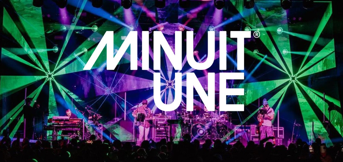 Das Bild zeigt eine beeindruckende Live-Bühnenszene mit einer dynamischen Lichtshow. Der Hintergrund ist von intensiven grünen und violetten Lichteffekten geprägt, die strahlenförmig von verschiedenen Punkten ausgehen und den gesamten Raum einhüllen.

In der Mitte des Bildes befindet sich das große, weiße Logo von Minuit Une, das prominent über die Szene gelegt wurde. Auf der Bühne stehen mehrere Musiker, die von einer aufwendigen Lichtinstallation umgeben sind.

Die Beleuchtung erzeugt eine immersive Atmosphäre, die typisch für die IVL-Technologie von Minuit Une ist. Die Kombination aus multidirektionalen Lichtstrahlen, Projektionen und der energiegeladenen Live-Performance vermittelt den Eindruck eines intensiven, mitreißenden Konzerterlebnisses.