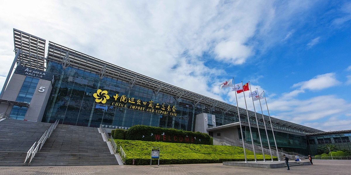 Canton Fair Complex Moderne Glasfassade des China Import & Export Fair Complex mit Treppe, Flaggenmasten und blauem Himmel.