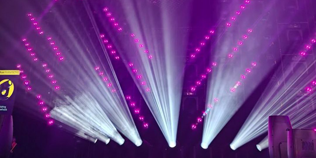 Violette und weiße Lichtstrahlen inszenieren eine Bühne mit dynamischen Effekten.