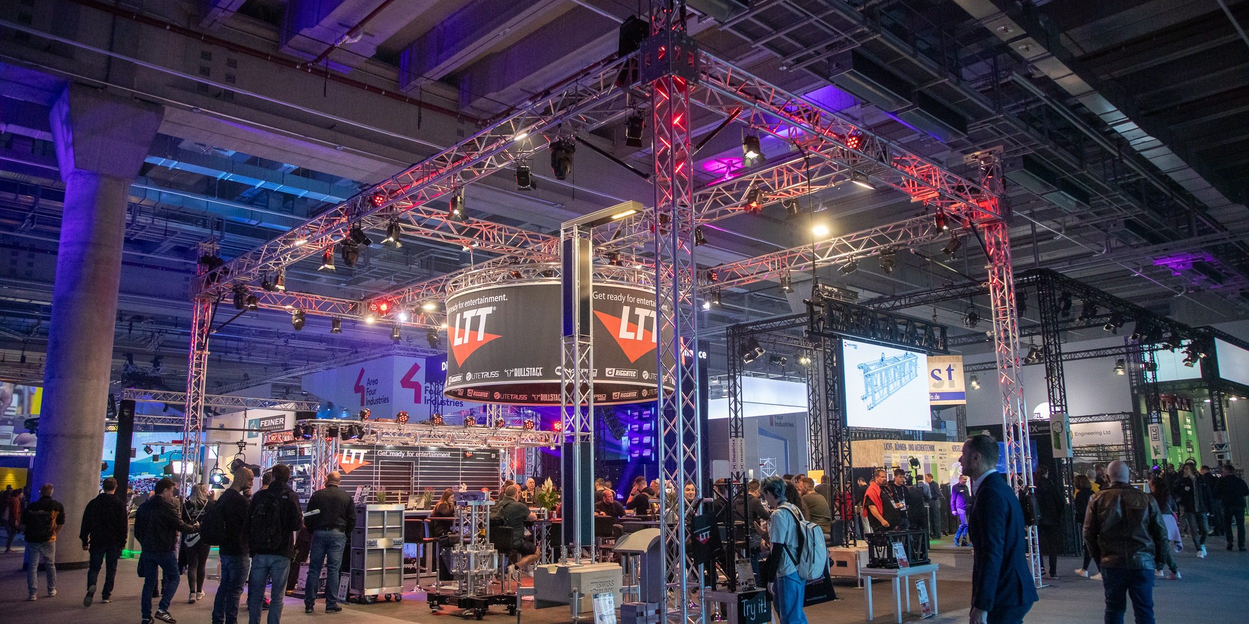 Menschen auf der Prolight + Sound Messehalle an einem beleuchteten Messestand von LTT