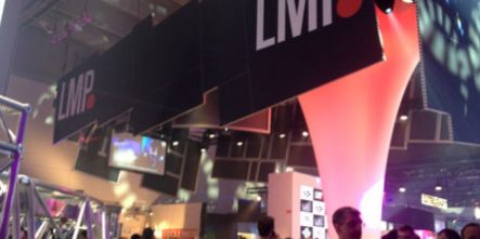 Messestand mit Beleuchtung, hängenden Displays und Besuchern in einer modernen Messehalle