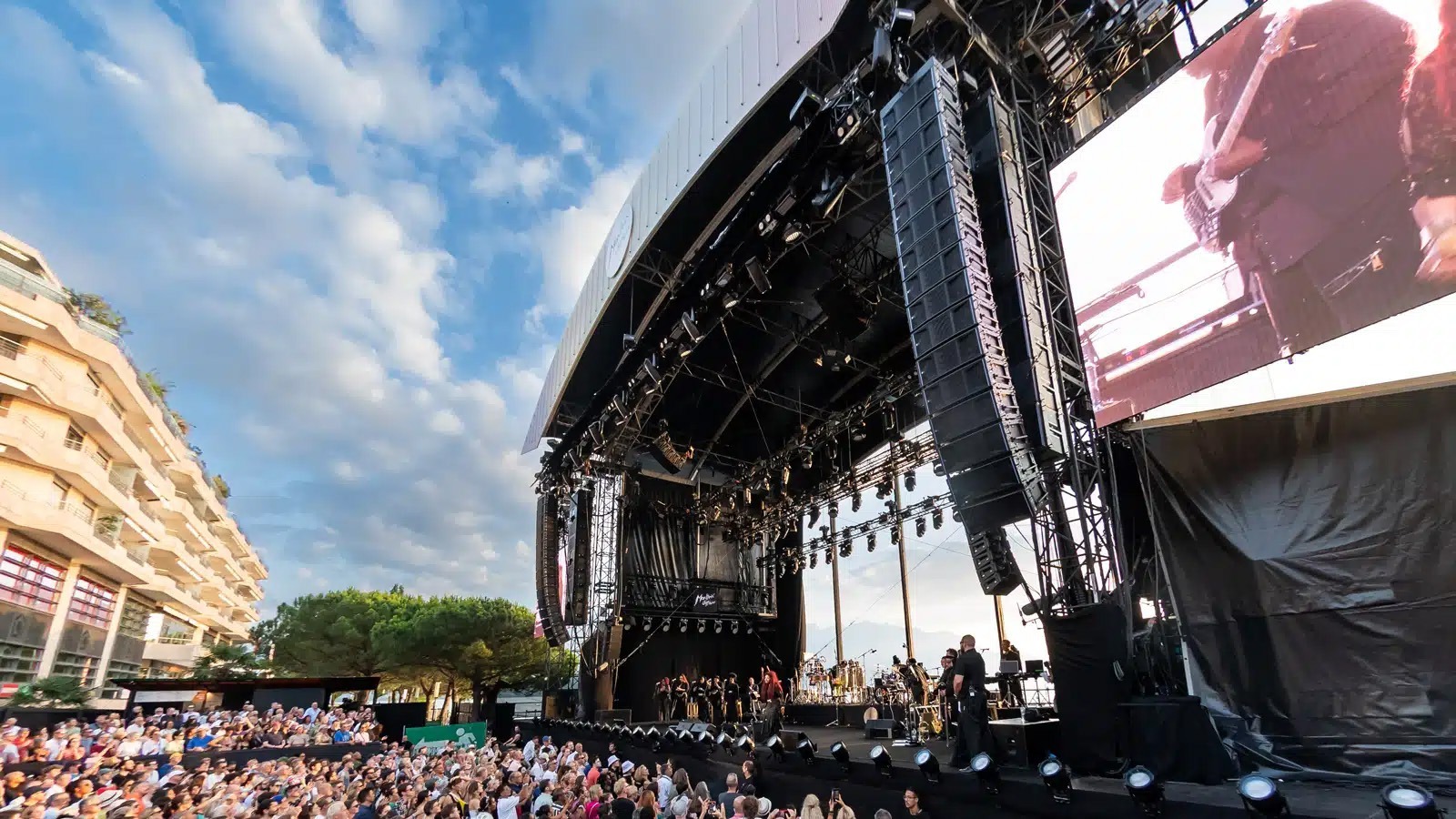 Open-Air-Bühne mit großen Lautsprecherarrays und Publikum bei sonnigem Wetter