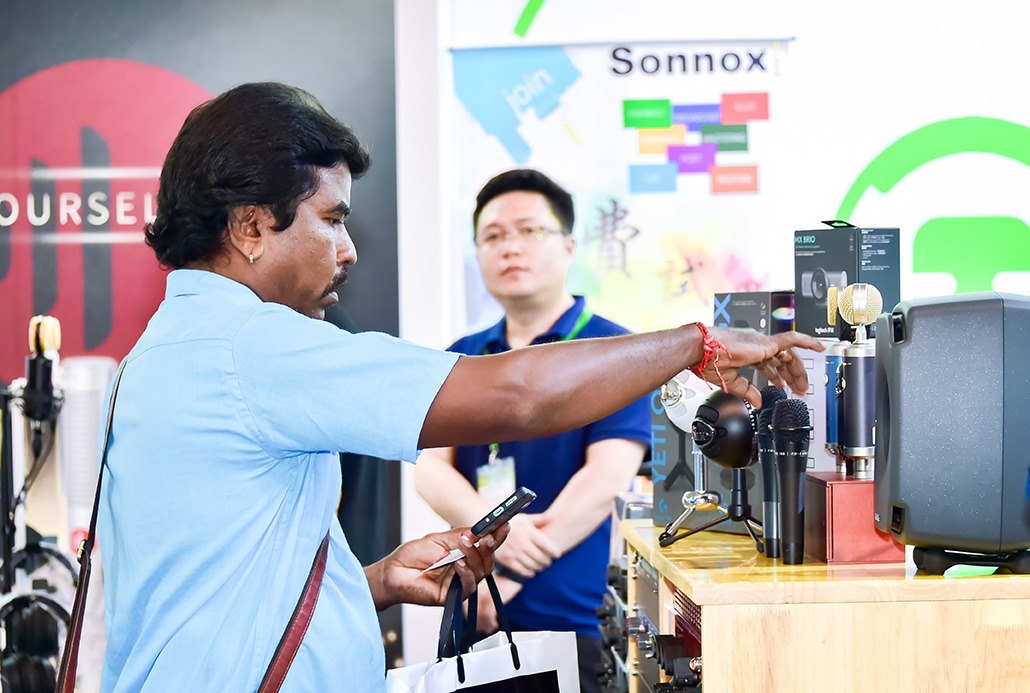 Besucher testet Mikrofone an Messestand, daneben Lautsprecher und Audioequipment