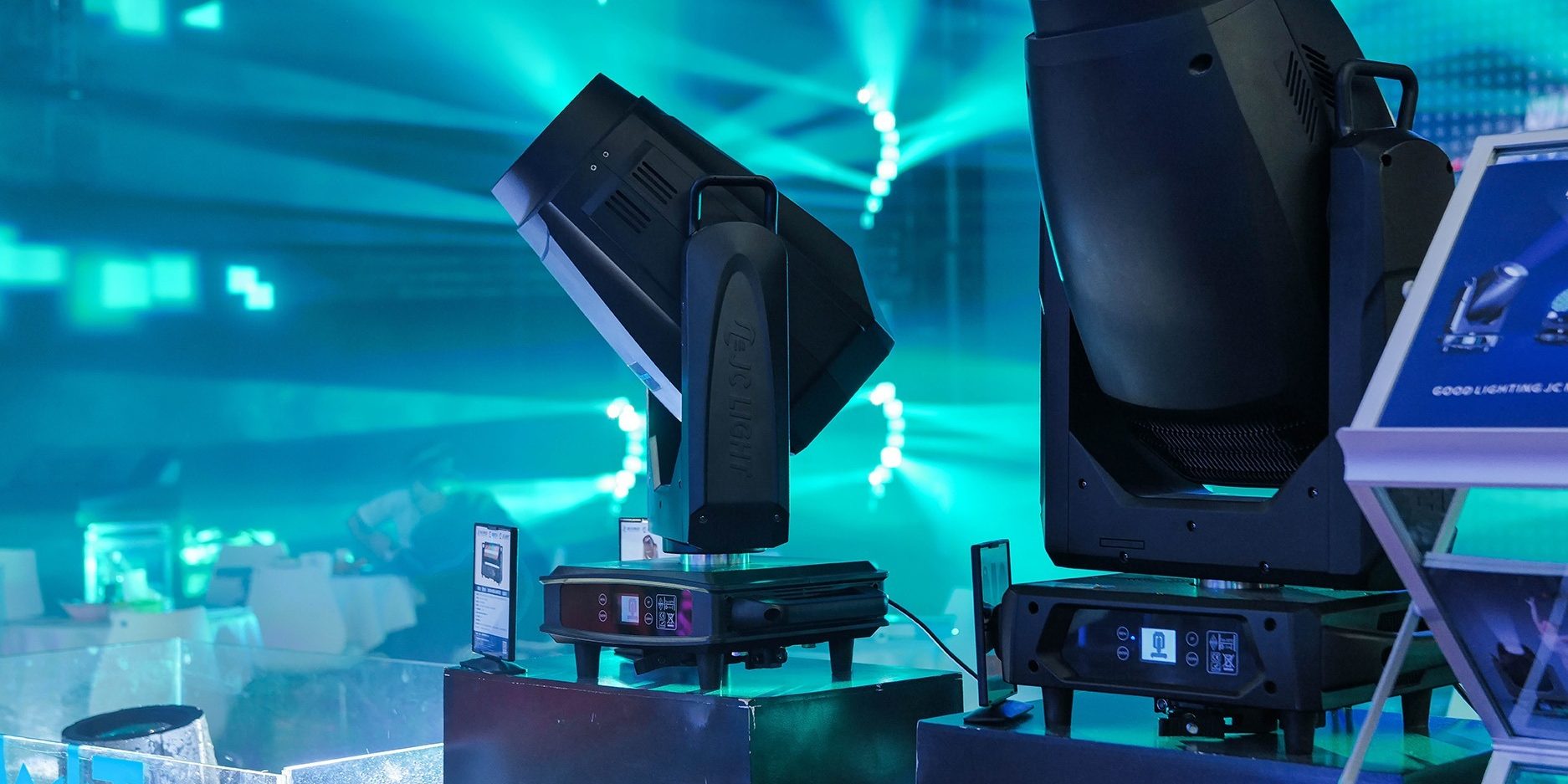 pro-light-exhibitor-plsb Professionelle Moving Lights erzeugen türkisfarbene Lichtstrahlen in einer Veranstaltungshalle.