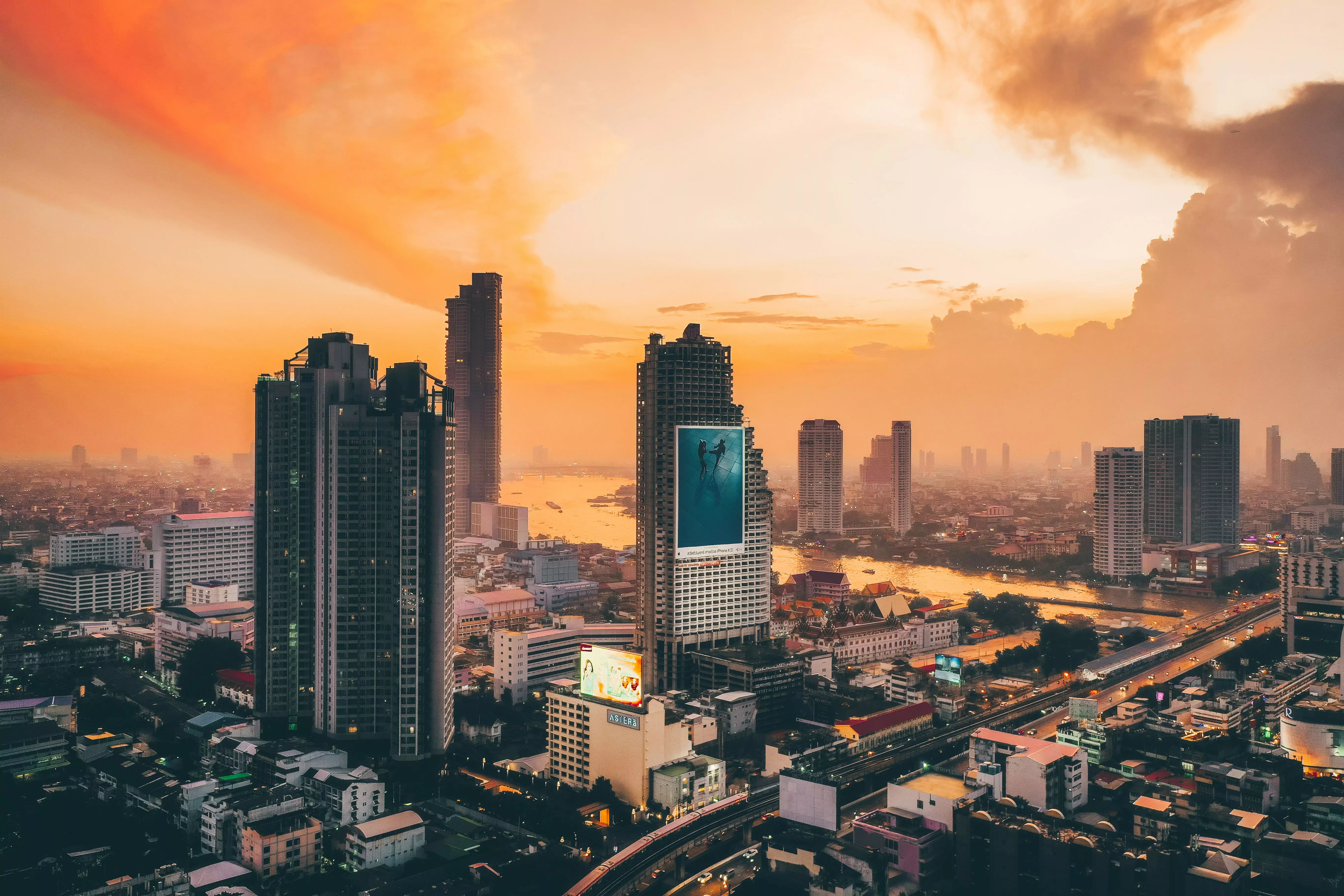 Bangkok-Skyline am Fluss bei Sonnenuntergang mit Hochhäusern und Straßen.