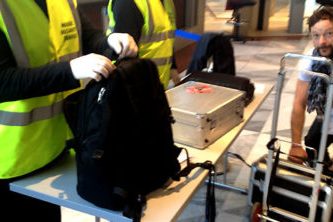 Sicherheitskontrolle mit Personal, das Rucksack und Technik an einem Eingang überprüft