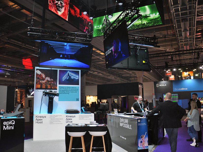 Messestand von Tait mit epiQ Mini Console, Bildschirmen und Besucherinnen und Besuchern auf Messe.