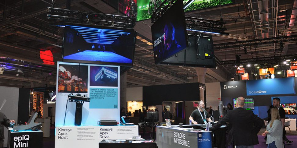 Messestand von Tait mit epiQ Mini Console, Bildschirmen und Besucherinnen und Besuchern auf Messe.