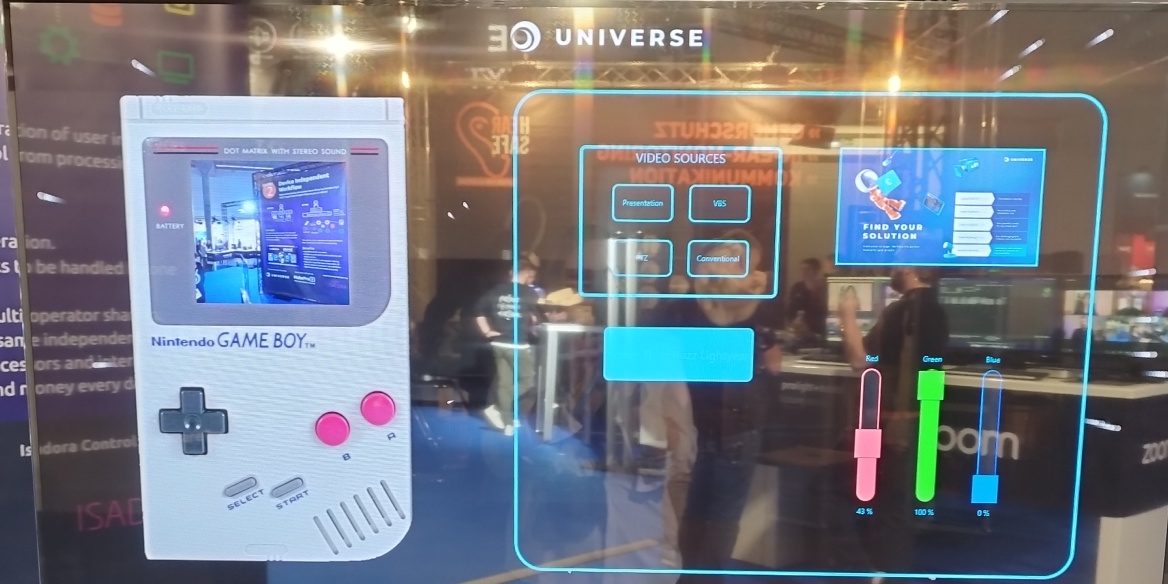 Universe Future Walk Das Bild zeigt ein interaktives Setup, das Retro-Technologie und moderne Steuerung kombiniert. Links ist ein Nintendo Game Boy zu sehen, dessen Bildschirm ein aktuelles Bild anzeigt, was auf eine kreative Nutzung als Interface hinweist. Rechts wird eine futuristische Benutzeroberfläche präsentiert, die verschiedene Bedienelemente umfasst, darunter Videoquellen-Auswahl und Schieberegler für Farbanpassungen (Rot, Grün, Blau) mit Prozentwerten. Im oberen Bereich ist eine Werbe- oder Infografik mit dem Slogan „Find Your Solution“ eingebettet. Der Hintergrund deutet auf eine Messe oder Ausstellung hin, mit Besuchern und einem Stand, der die Interaktion zwischen Technologie und Kreativität hervorhebt.