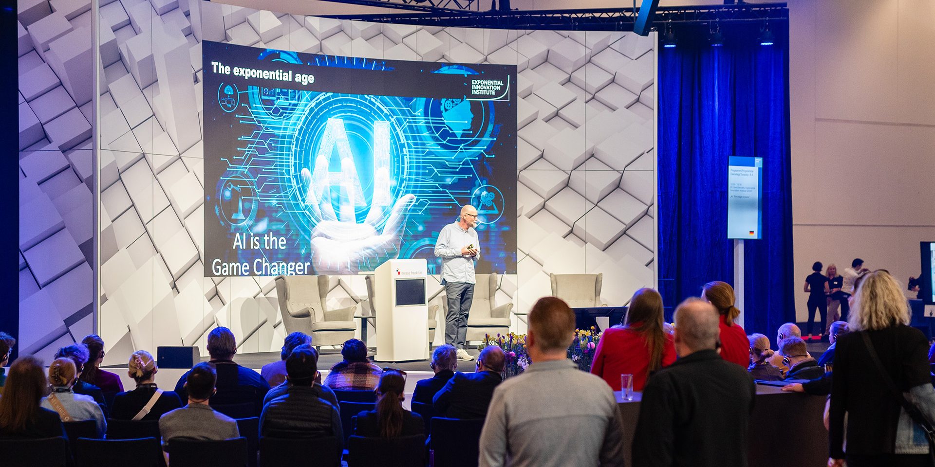 Uve Samuels Keynote: AI Gamechanger Ein Redner präsentiert auf einer Bühne zum Thema KI vor einem aufmerksam lauschenden Publikum.