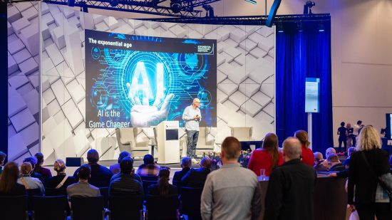 Ein Redner präsentiert auf einer Bühne zum Thema KI vor einem aufmerksam lauschenden Publikum.