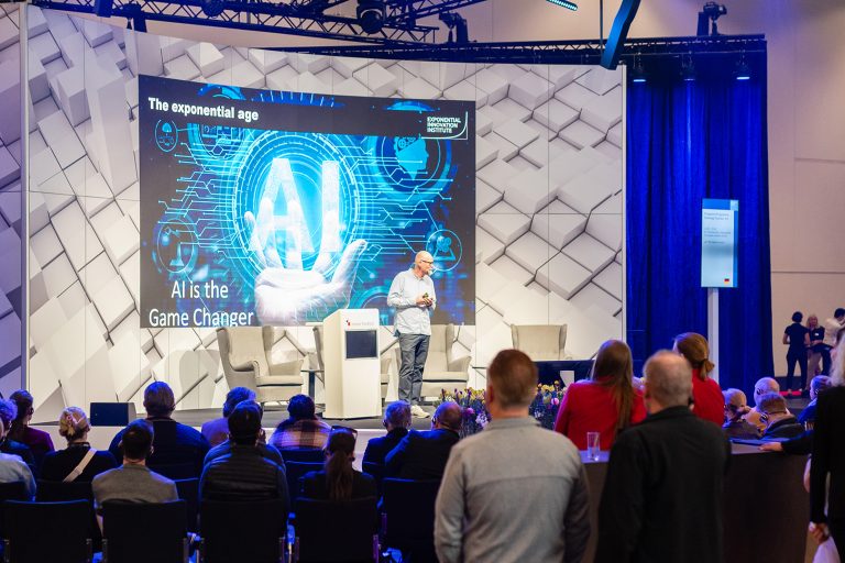 Uve Samuels Keynote: AI Gamechanger Ein Redner präsentiert auf einer Bühne zum Thema KI vor einem aufmerksam lauschenden Publikum.